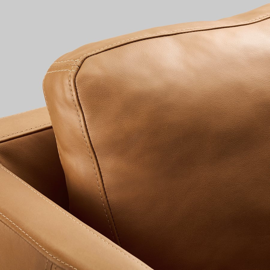 Close-up of a brown leather armchair with visible stitching.