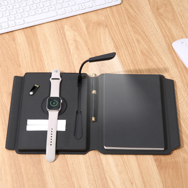 Black open notebook with a smartwatch, pen, and small lamp on a wooden desk.