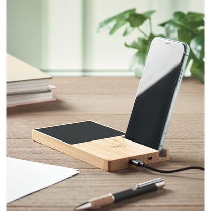 Wooden phone stand with smartphone on a desk with books and plants in the background