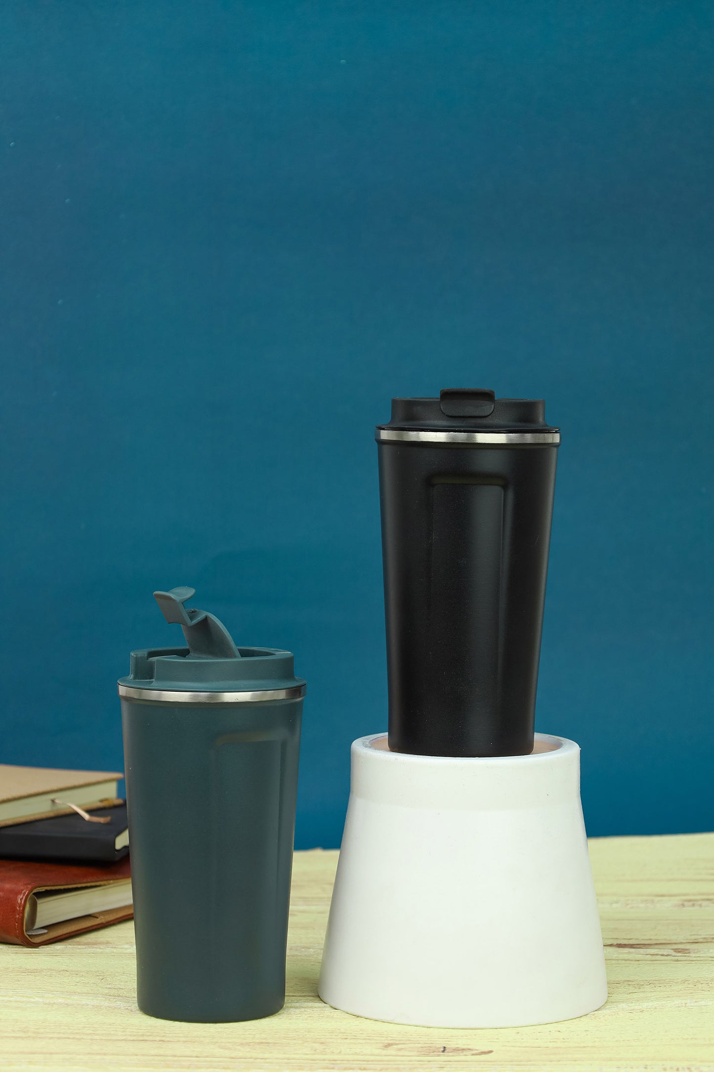 Two travel mugs, one black and one gray, on a wooden surface with a blue background.