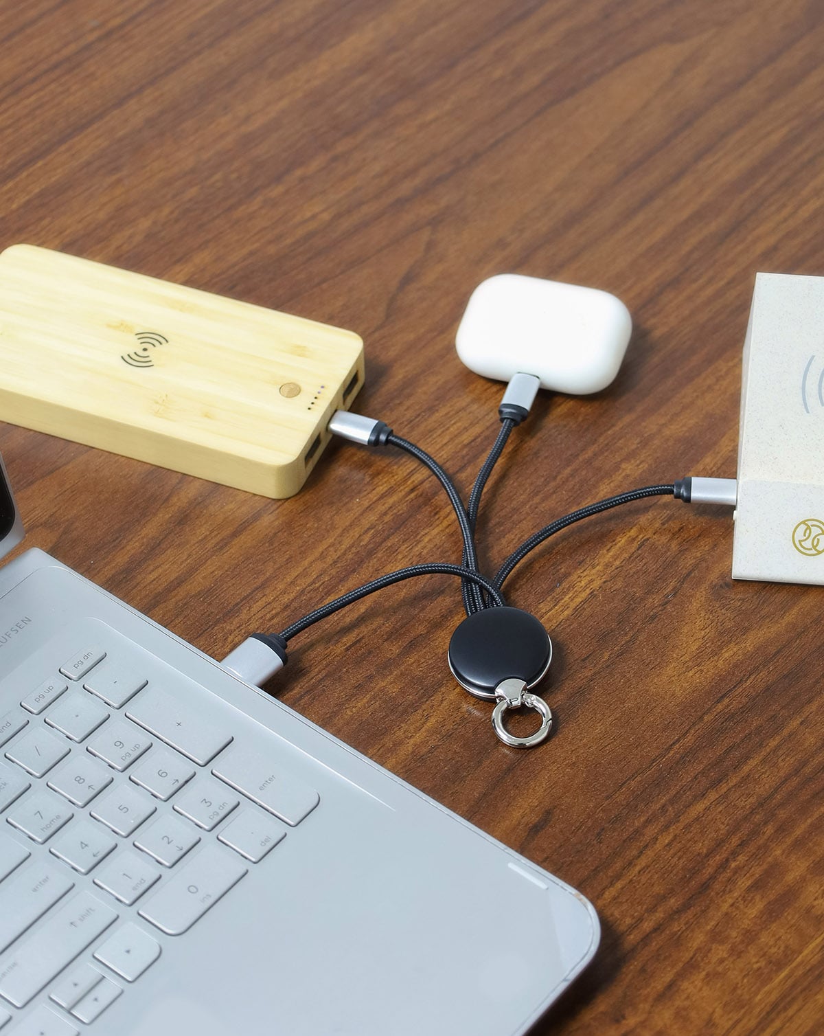 Wireless charging pad, power bank, and phone on a wooden surface with a laptop.