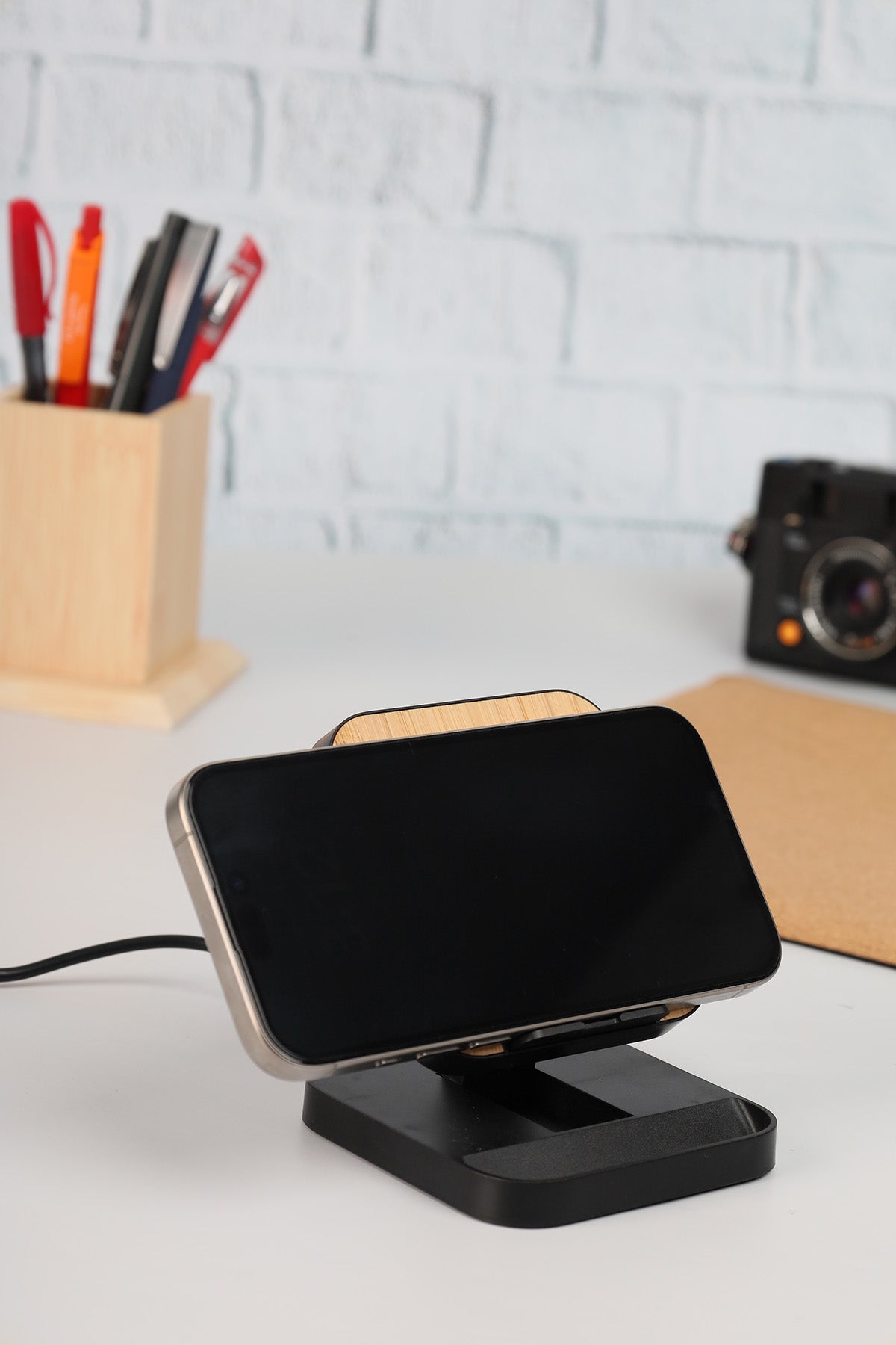 Black smartphone stand with a phone on a white surface, with a light gray brick wall in the background.