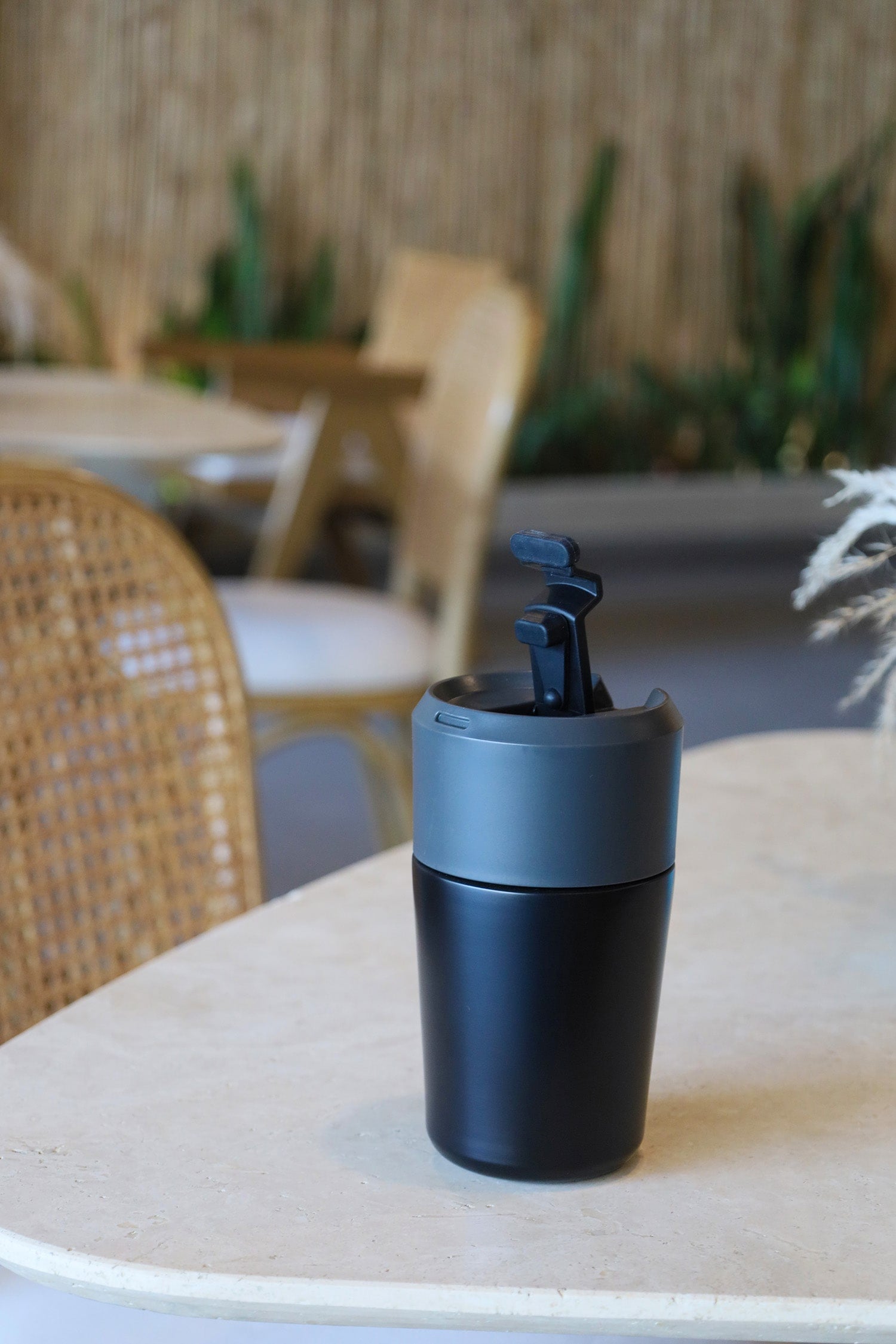 Black travel mug on a table with a blurred outdoor setting