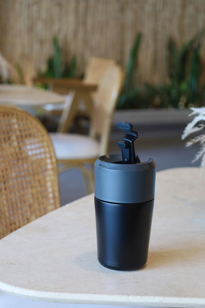 Black travel mug on a table with a blurred outdoor setting