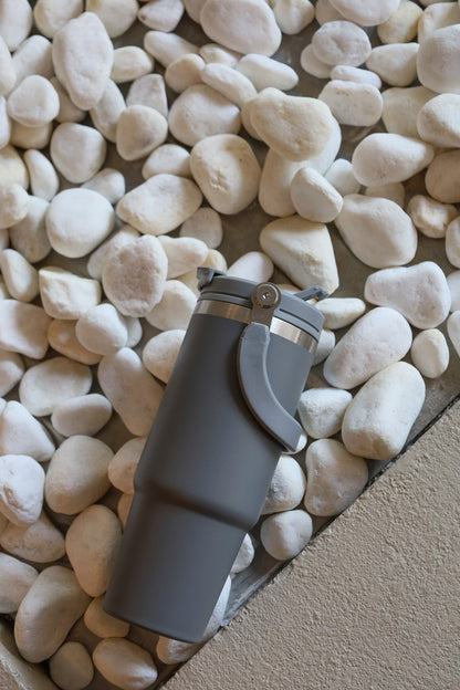 Gray water bottle with a black cap on pebbles