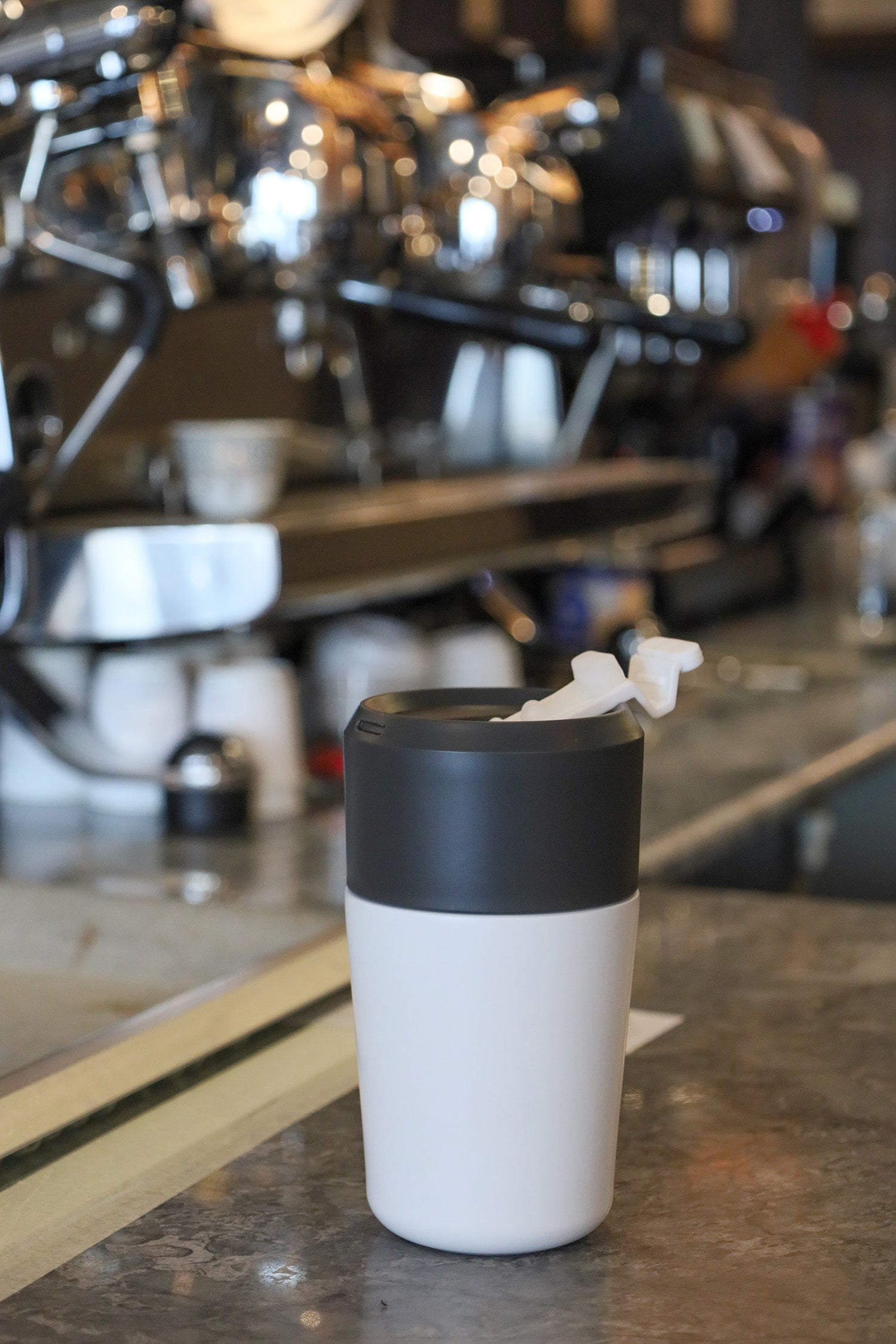 White coffee cup with black lid on a counter in a coffee shop setting