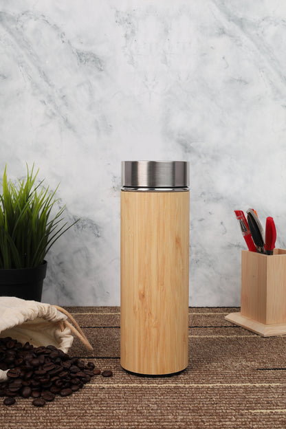 Bamboo tumbler with silver lid on a wooden surface with coffee beans and a plant in the background.