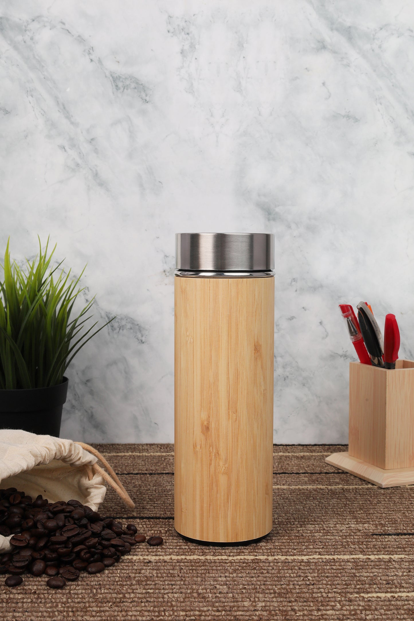 Bamboo tumbler with silver lid on a wooden surface with coffee beans and a plant in the background.