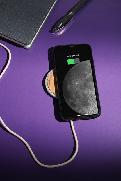 Smartphone on a wireless charger with a moon phase display on a purple surface.