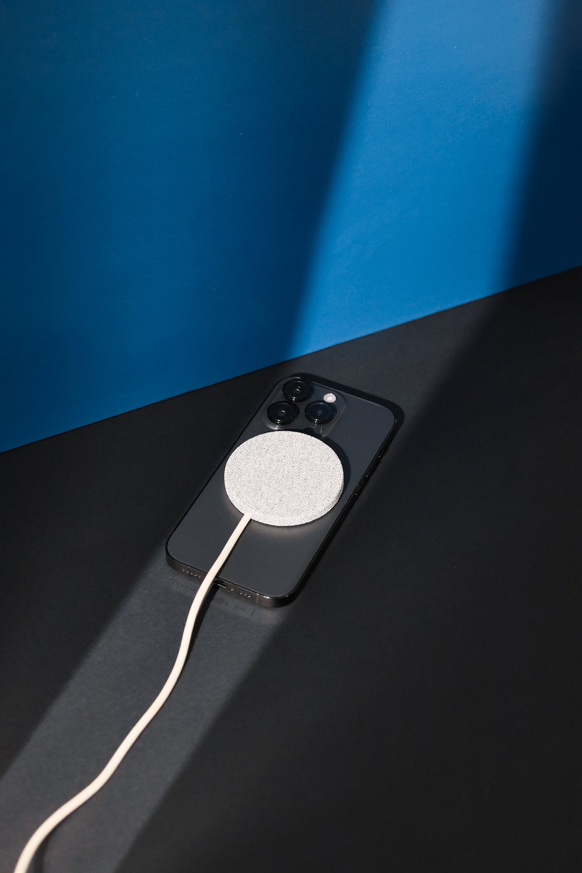 Phone with a white charging cable on a black surface against a blue wall