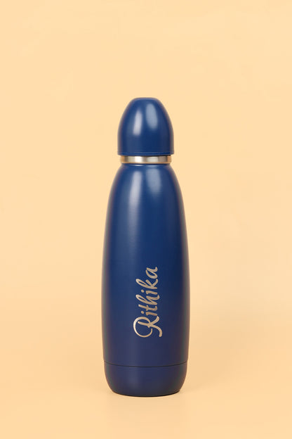 Blue water bottle with 'Ritika' engraving on a beige background
