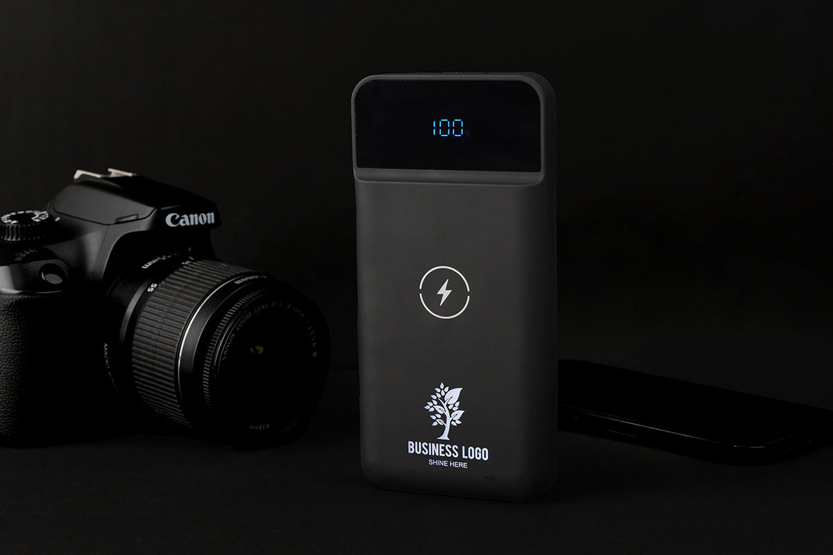 Black power bank with digital display next to a Canon camera on a dark background