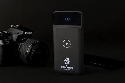 Black power bank with digital display next to a Canon camera on a dark background