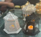 Two small lanterns with candles inside on a reflective surface.