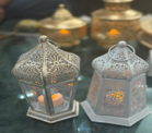 Decorative metal lanterns with candles inside on a reflective surface