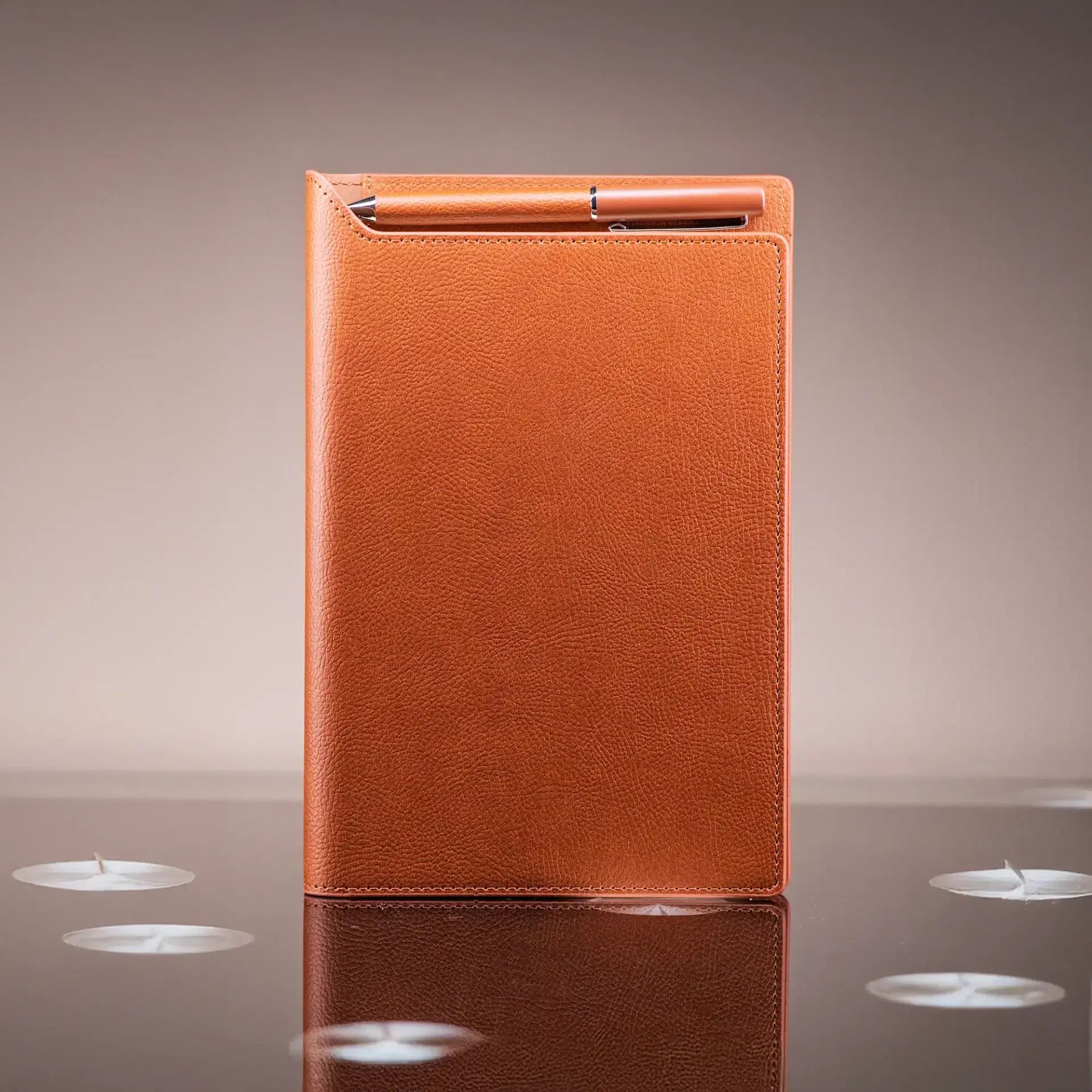 Brown leather notebook with a pen on a reflective surface