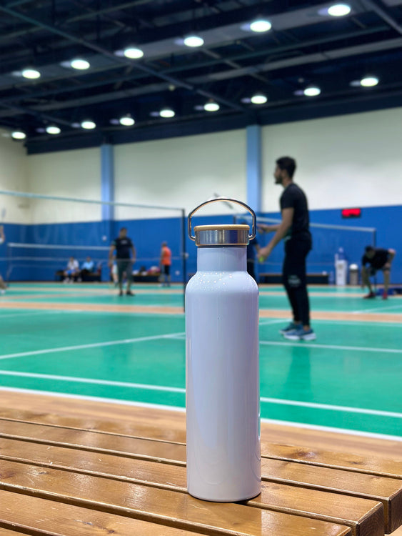 White water bottle with gold cap on a wooden bench in a badminton court.